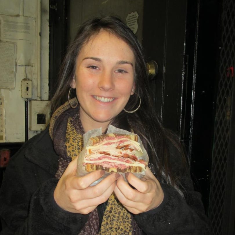 A smiling woman holds a large, meat-filled sandwich from Koch's Deli.