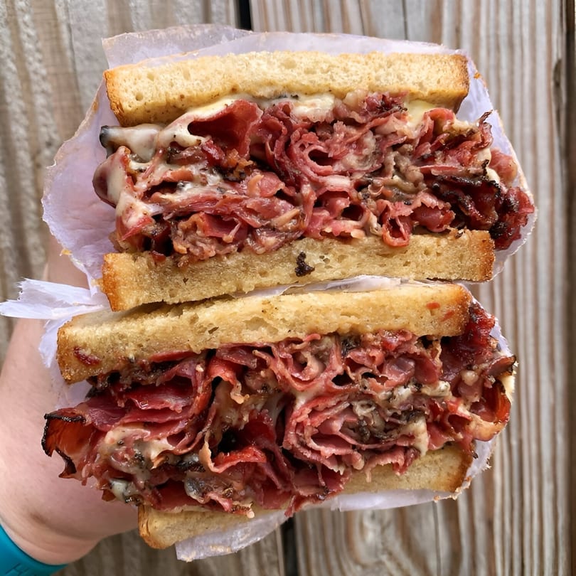 A large, sliced deli sandwich with abundant pastrami and melted cheese on toasted bread.