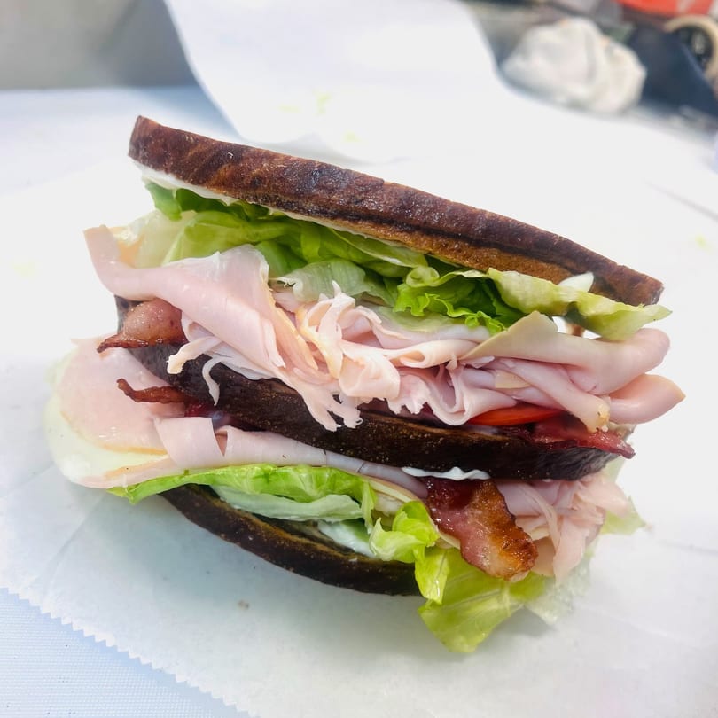 A large deli club sandwich with turkey, bacon, lettuce, and tomato on dark bread.