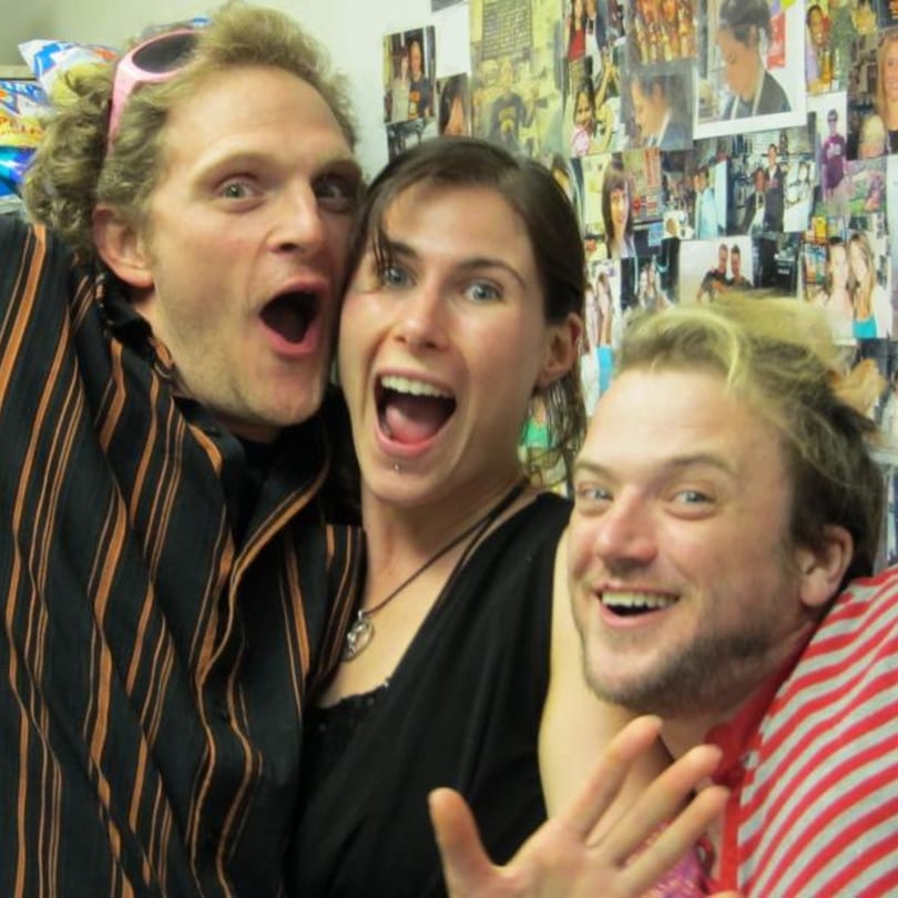 Three excited people with open mouths and wide eyes, posing in front of a wall covered in photos.