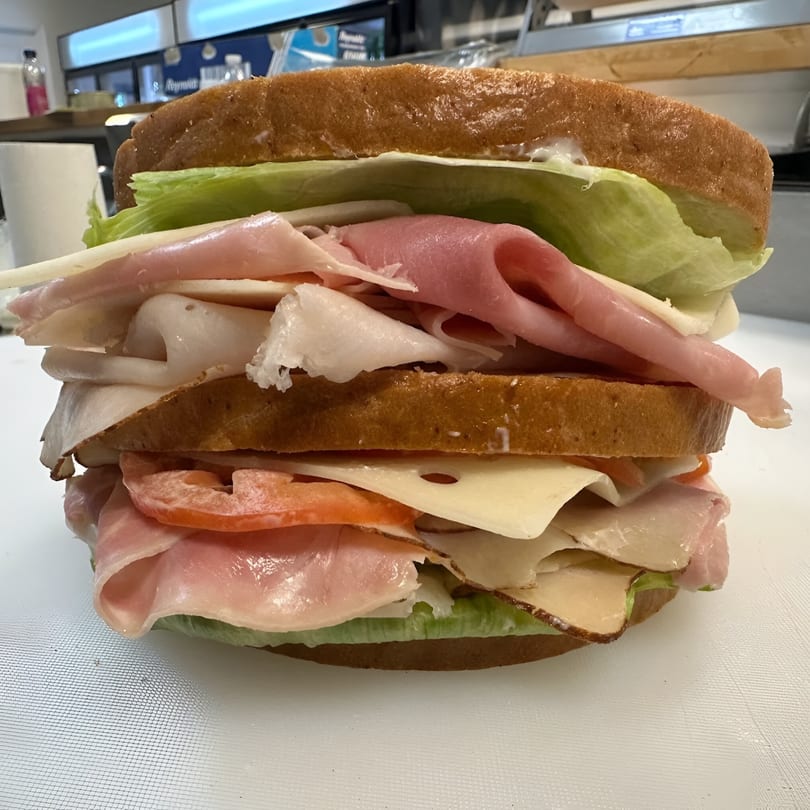 A towering deli sandwich from Koch's Deli, packed with various meats, cheese, lettuce, and tomato.