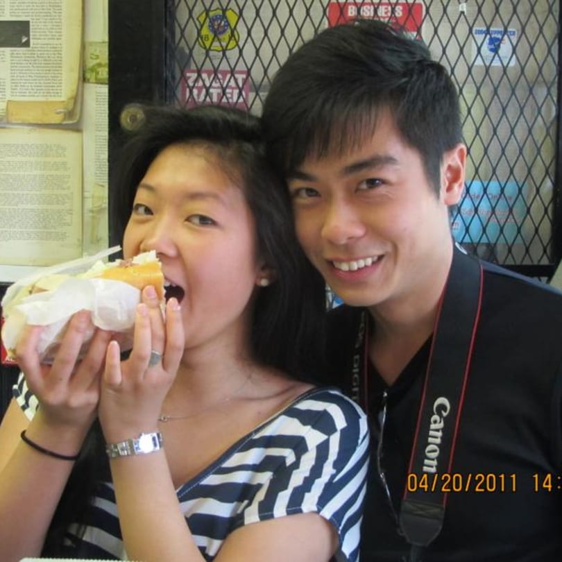 A woman bites into a large sandwich while a man smiles beside her at Koch's Deli.