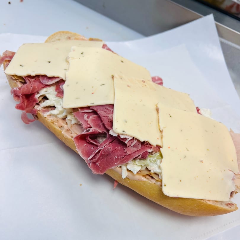 A large deli sandwich from Koch's Deli, filled with meat, cheese, and coleslaw on a white paper.