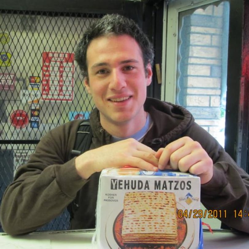 A young man smiling with a box of Yehuda Matzos in front of him at Koch's Deli.